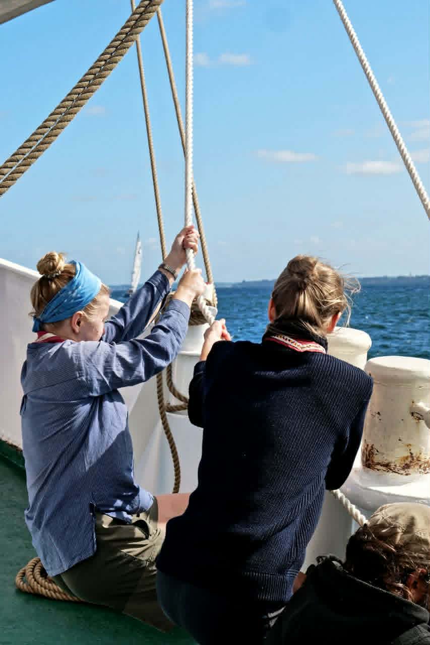Two crew members hauling lines together aboard a traditional sailing ship during Seamanship Academy training